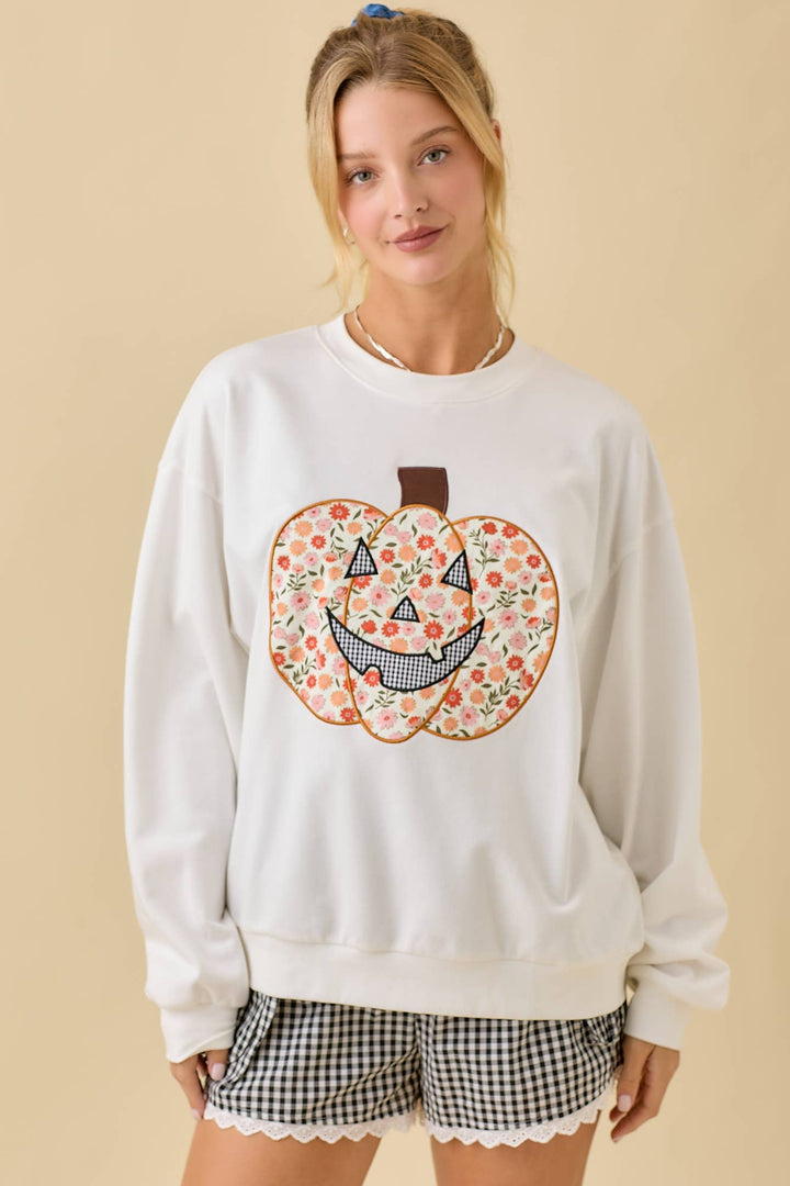 Woman wearing a white sweatshirt with a floral pumpkin design on a beige background