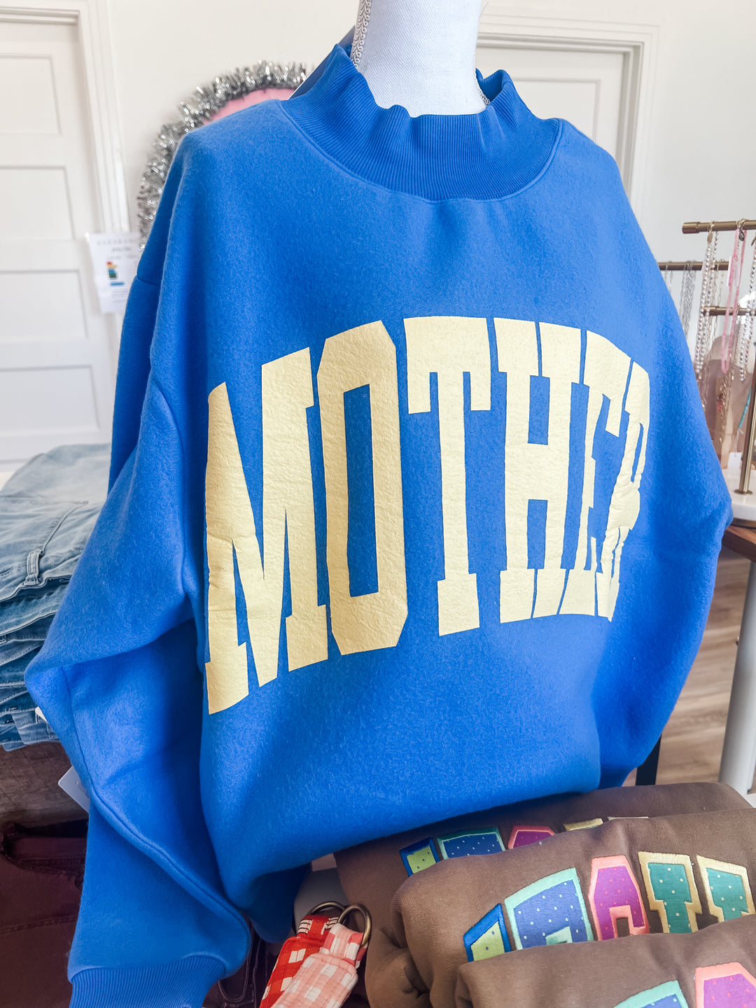 Blue mock neck sweatshirt with “mother” text in a butter yellow 