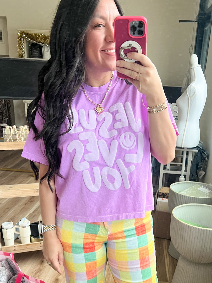 Woman wearing a purple t-shirt with “Jesus Loves You” 