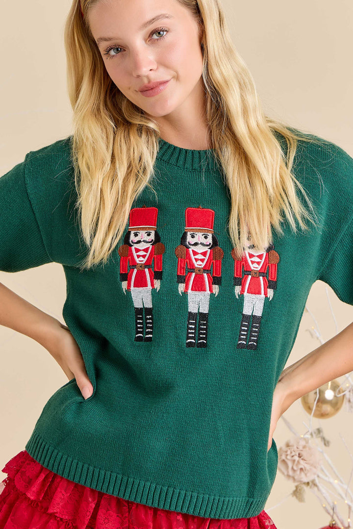 Woman wearing a green sweater with nutcracker designs on a beige background