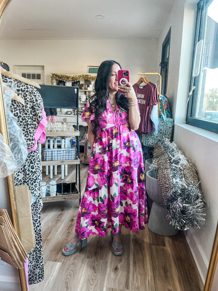 Woman in a pink floral dress taking a mirror selfie in a room with clothing and decor.