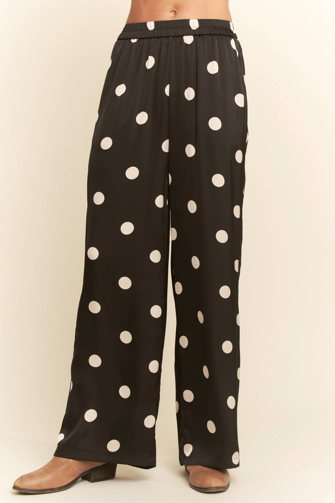 Black pants with white polka dots worn by a person on a beige background