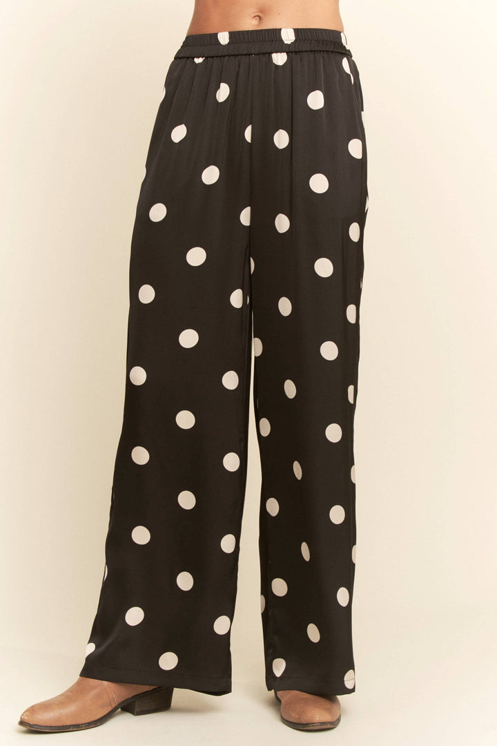 Black pants with white polka dots worn by a person on a beige background
