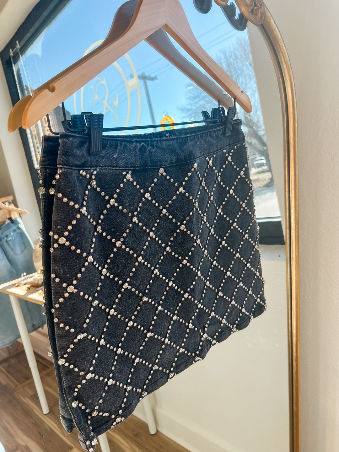 Black skirt with white rhinestone  pattern hanging on a hanger in front of a mirror.