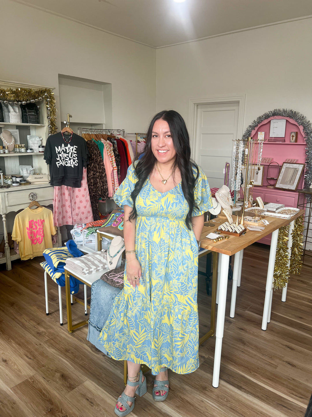 Woman in a yellow and blue cotton midi dress standing in a store with various items on display.