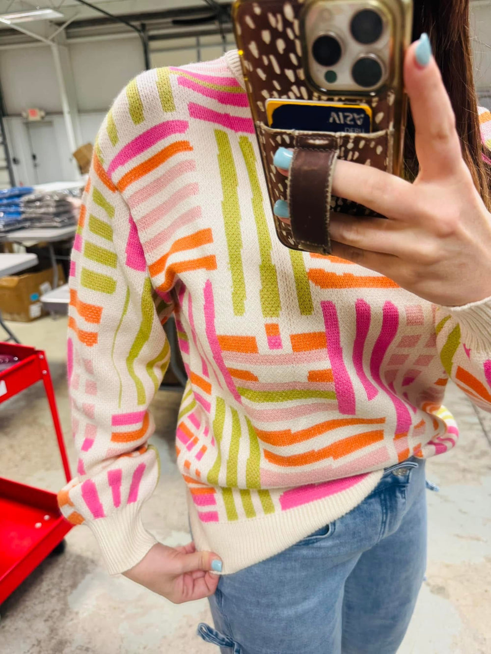 Person wearing a colorful striped sweater taking a mirror selfie.