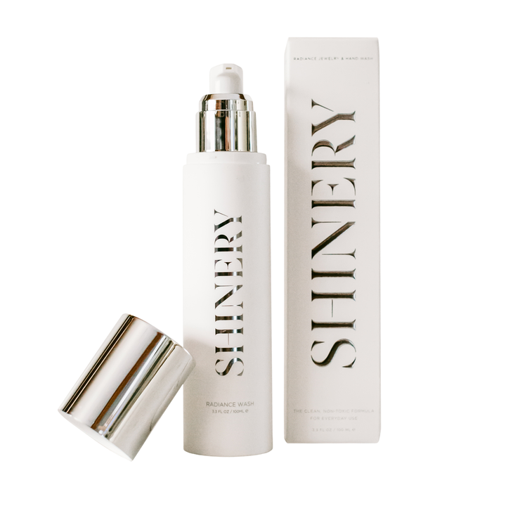 A bottle of Jewelry Wash luxury jewelry cleaner with its packaging box, both featuring a white color scheme with metallic elements.