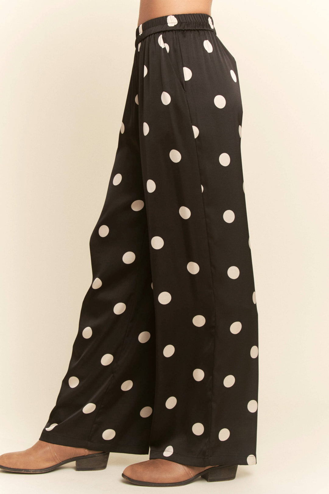 Black wide-leg pants with white polka dots on a beige background