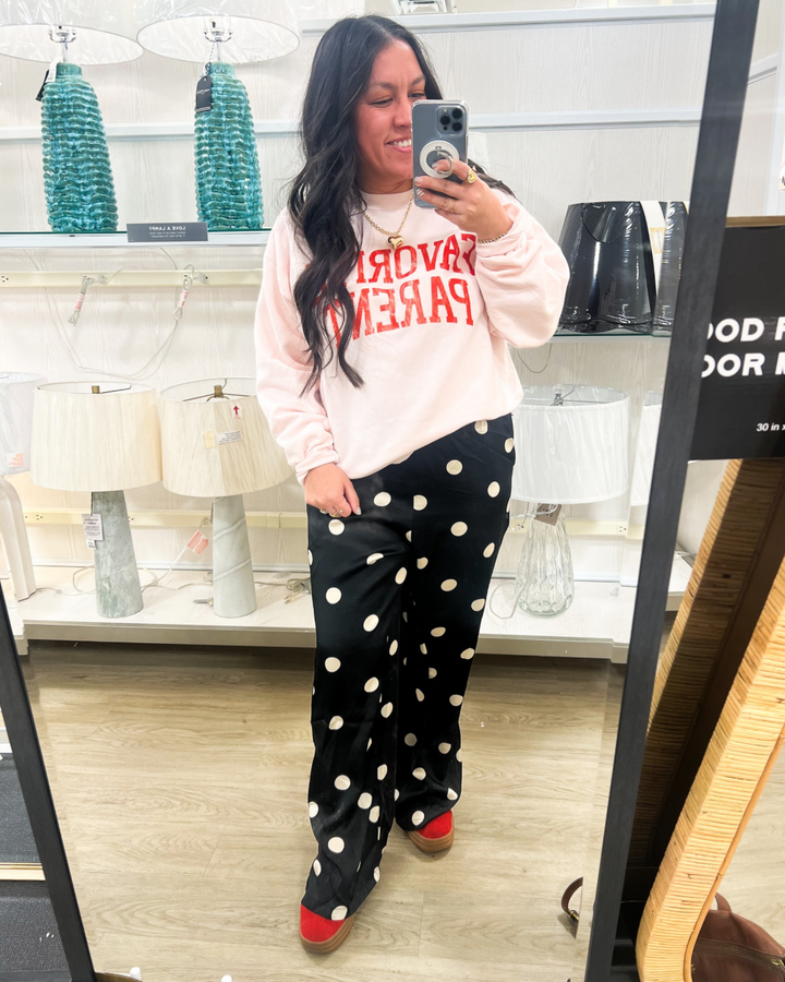 woman waring a light pink sweatshirt with text "FAVORITE PARENT" and black pants with white polka dots