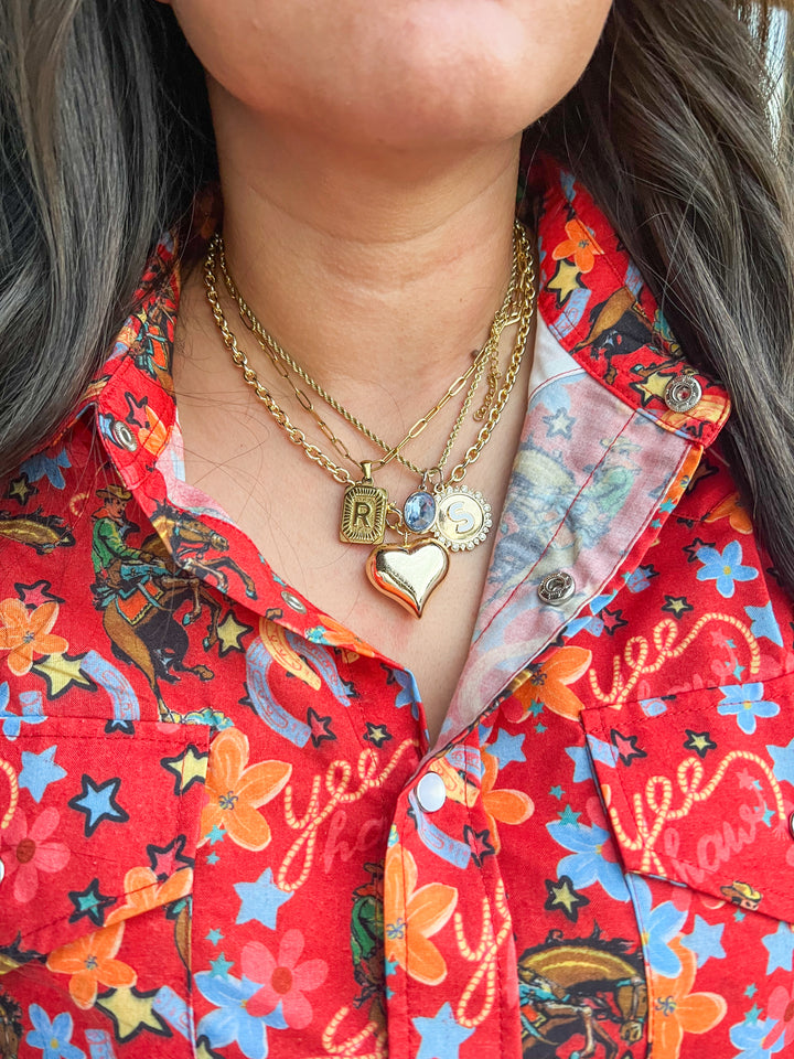 Person wearing a colorful shirt with floral patterns and gold necklaces.