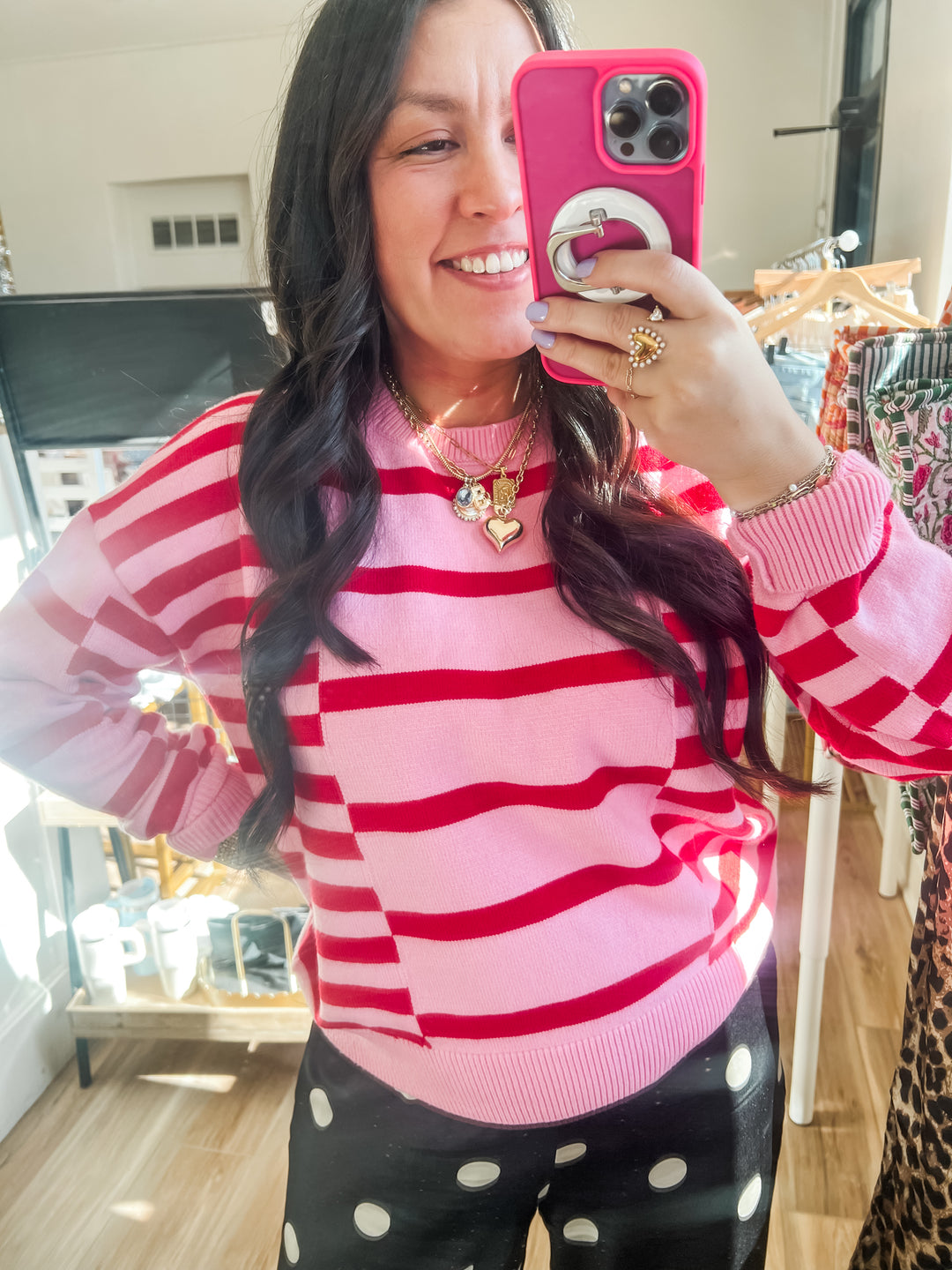 Woman taking a mirror selfie wearing a pink and red striped sweater and black polka dot pants.