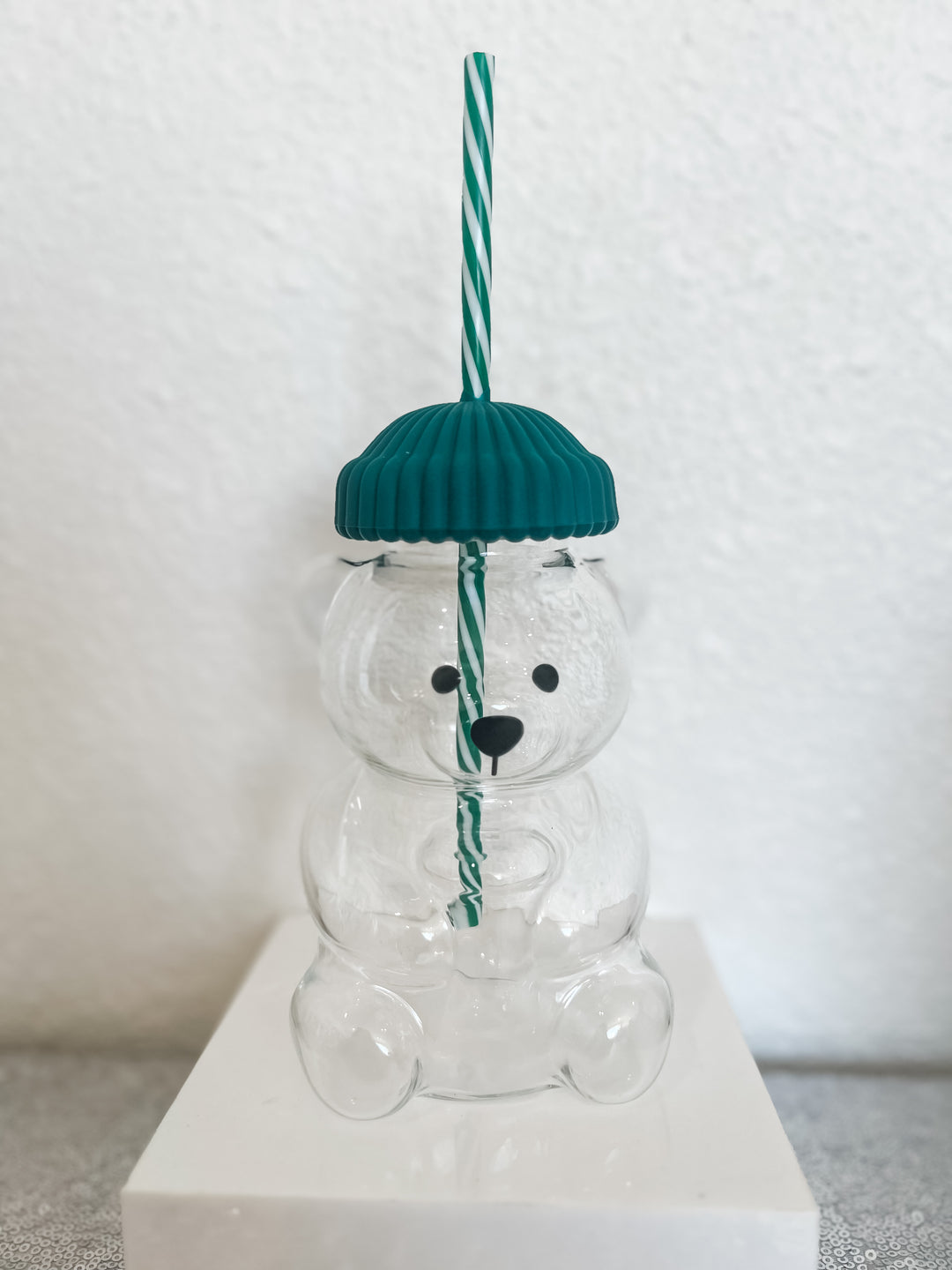 Clear glass bear with a green hat and straw 