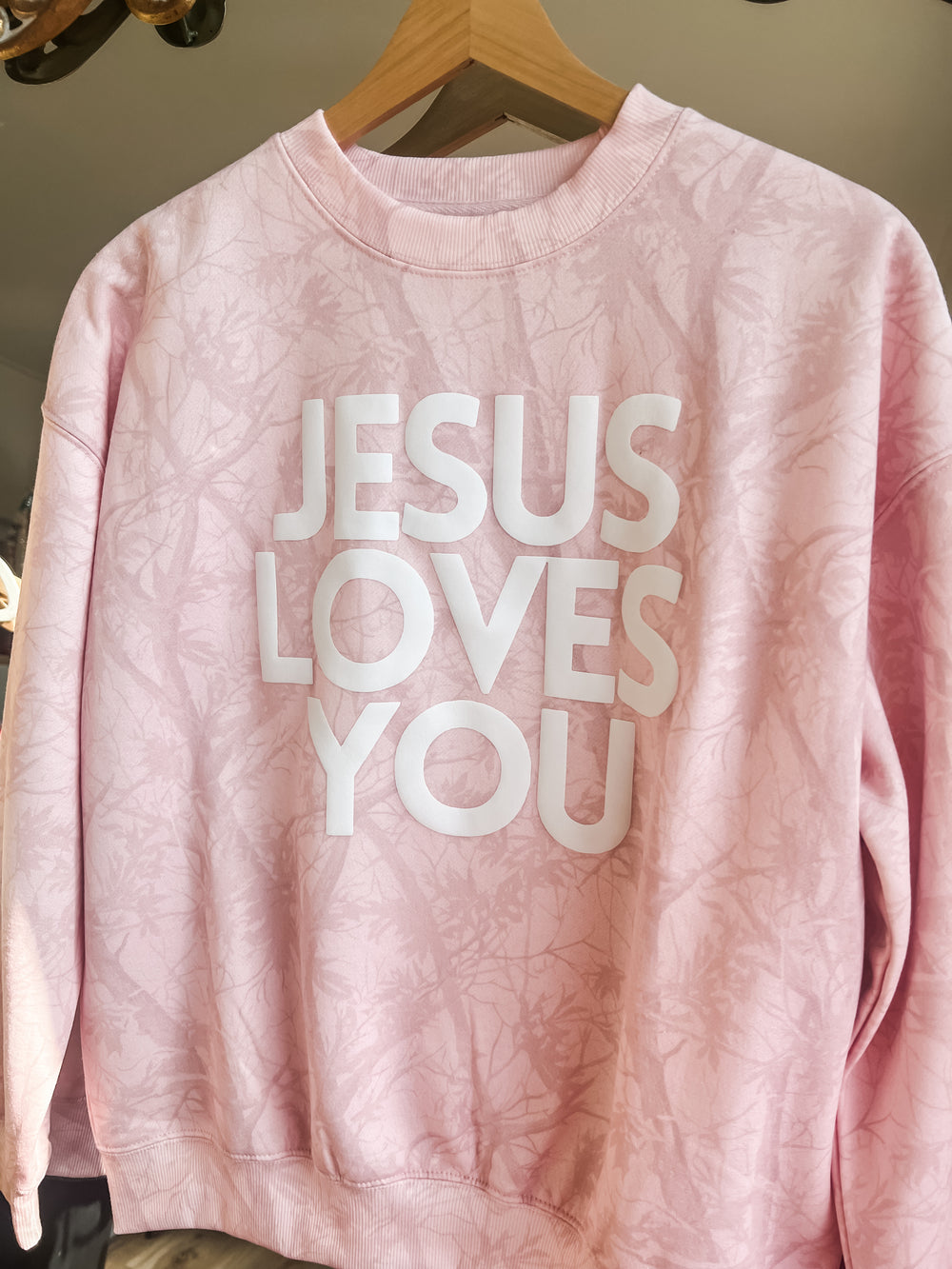 Pink sweatshirt with 'Jesus Loves You' text on a hanger