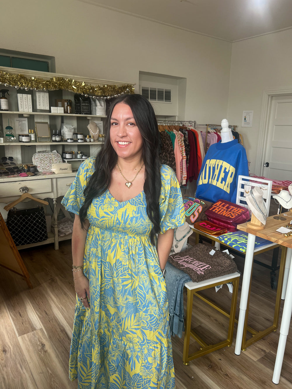 Woman in a blue and yellow midi smocked dress standing in a room with shelves and furniture.