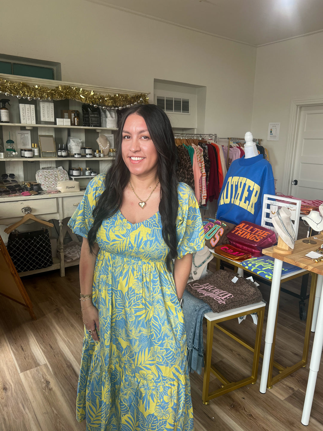 Woman in a blue and yellow midi smocked dress standing in a room with shelves and furniture.