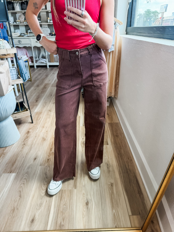 A person taking a mirror selfie in a boutique, wearing high-waisted, wide-leg brown corduroy pants, a red tank top, and white sneakers.