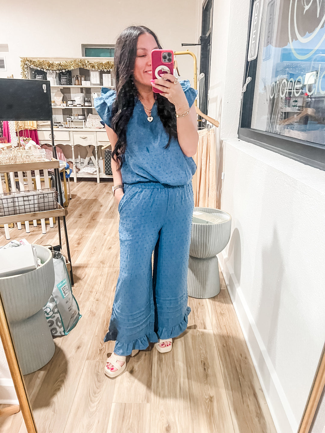 Woman taking a mirror selfie wearing a blue two piece set in a store. 