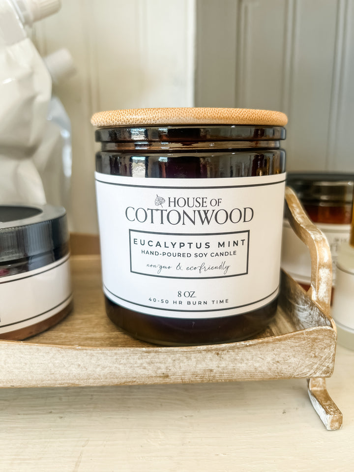 A dark amber glass jar candle with a bamboo-style lid and a white label reading &