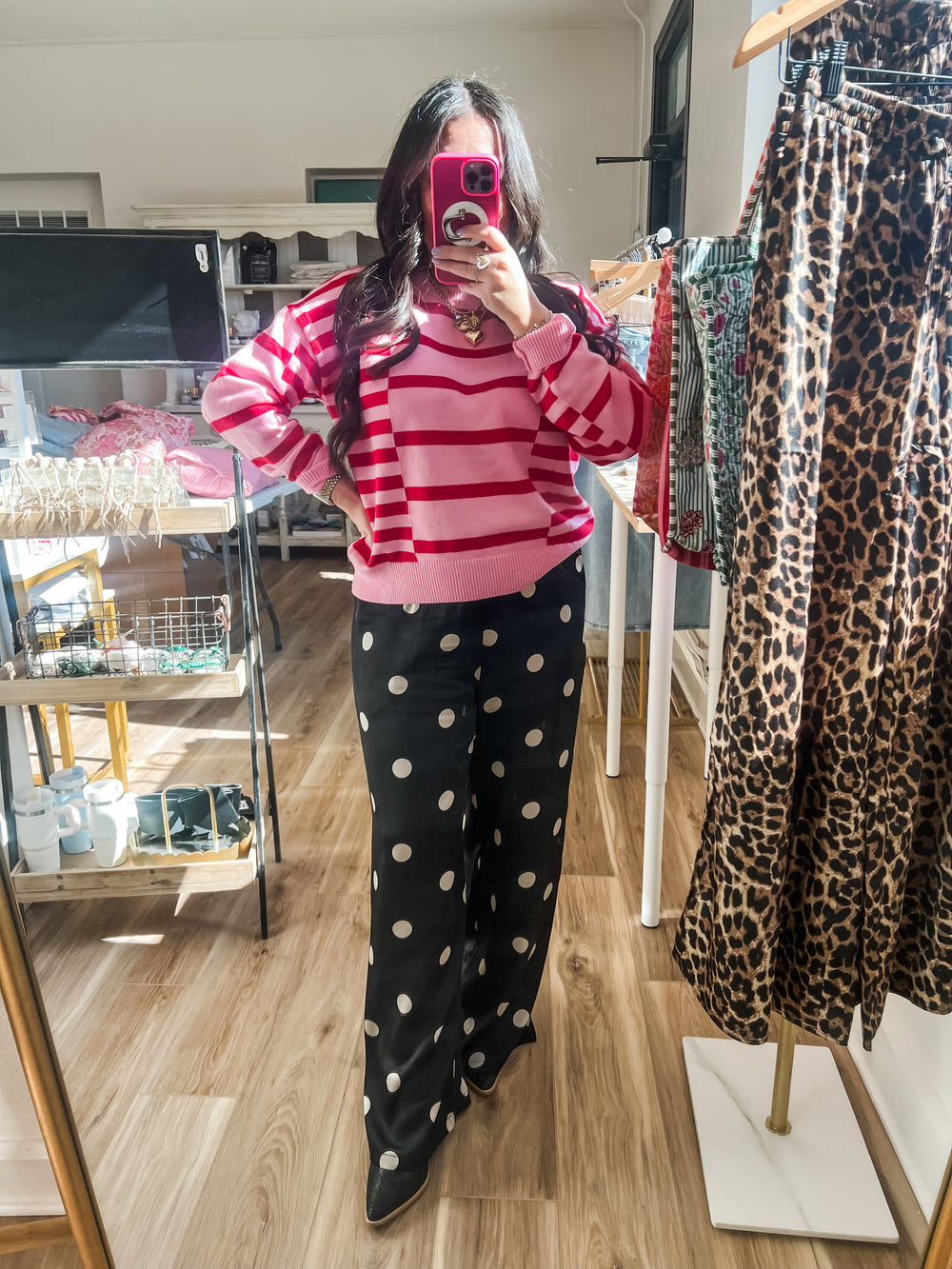 Person wearing a pink and red striped sweater and black polka dot pants taking a mirror selfie.