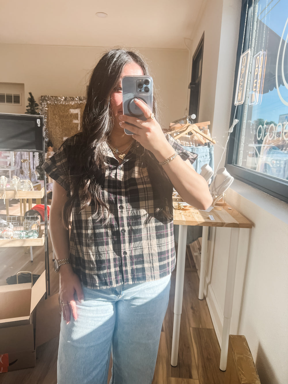 Person taking a mirror selfie wearing a plaid shirt and jeans