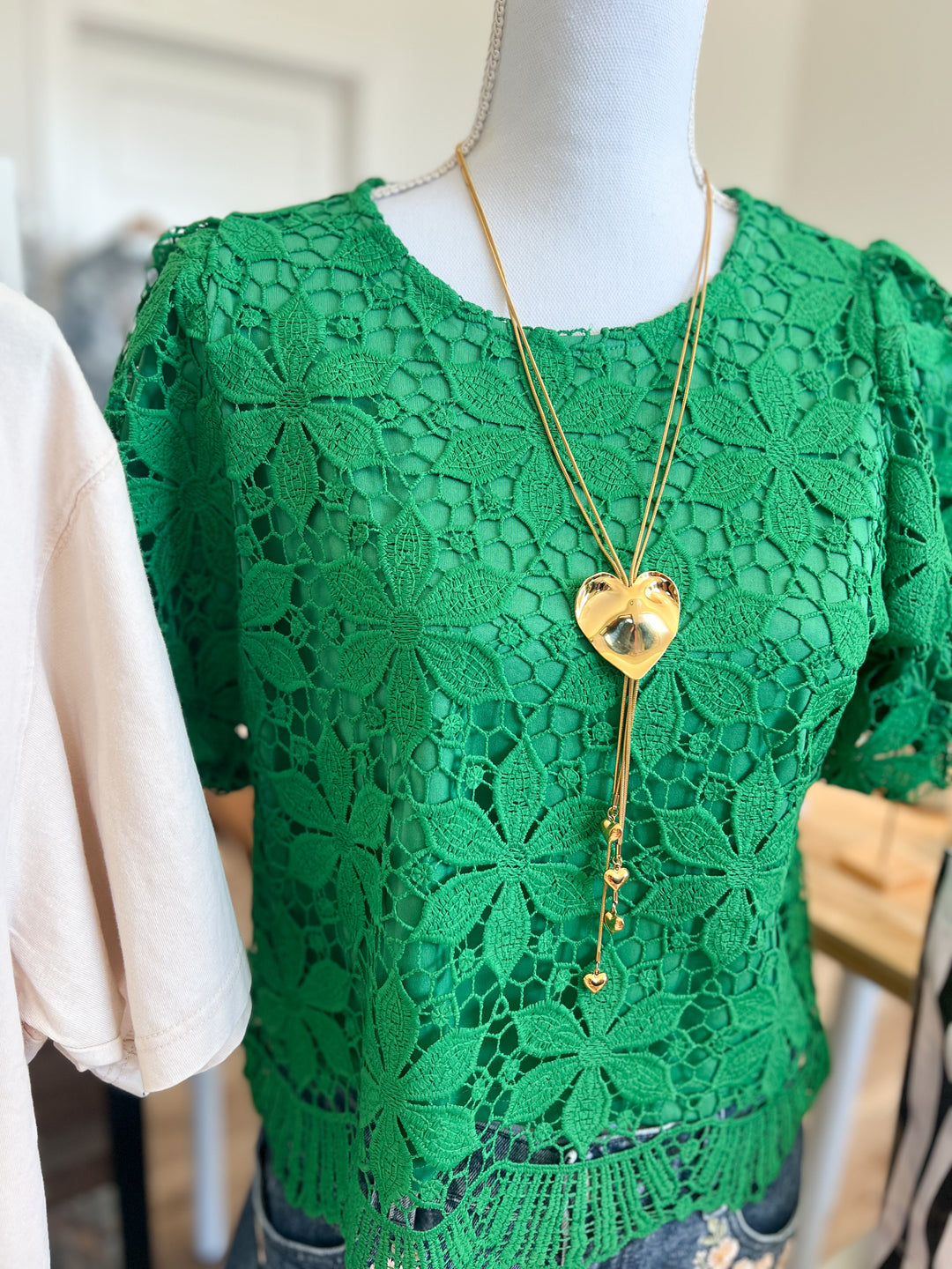A bright green short-sleeve lace top displayed on a mannequin, styled with a gold heart pendant necklace.