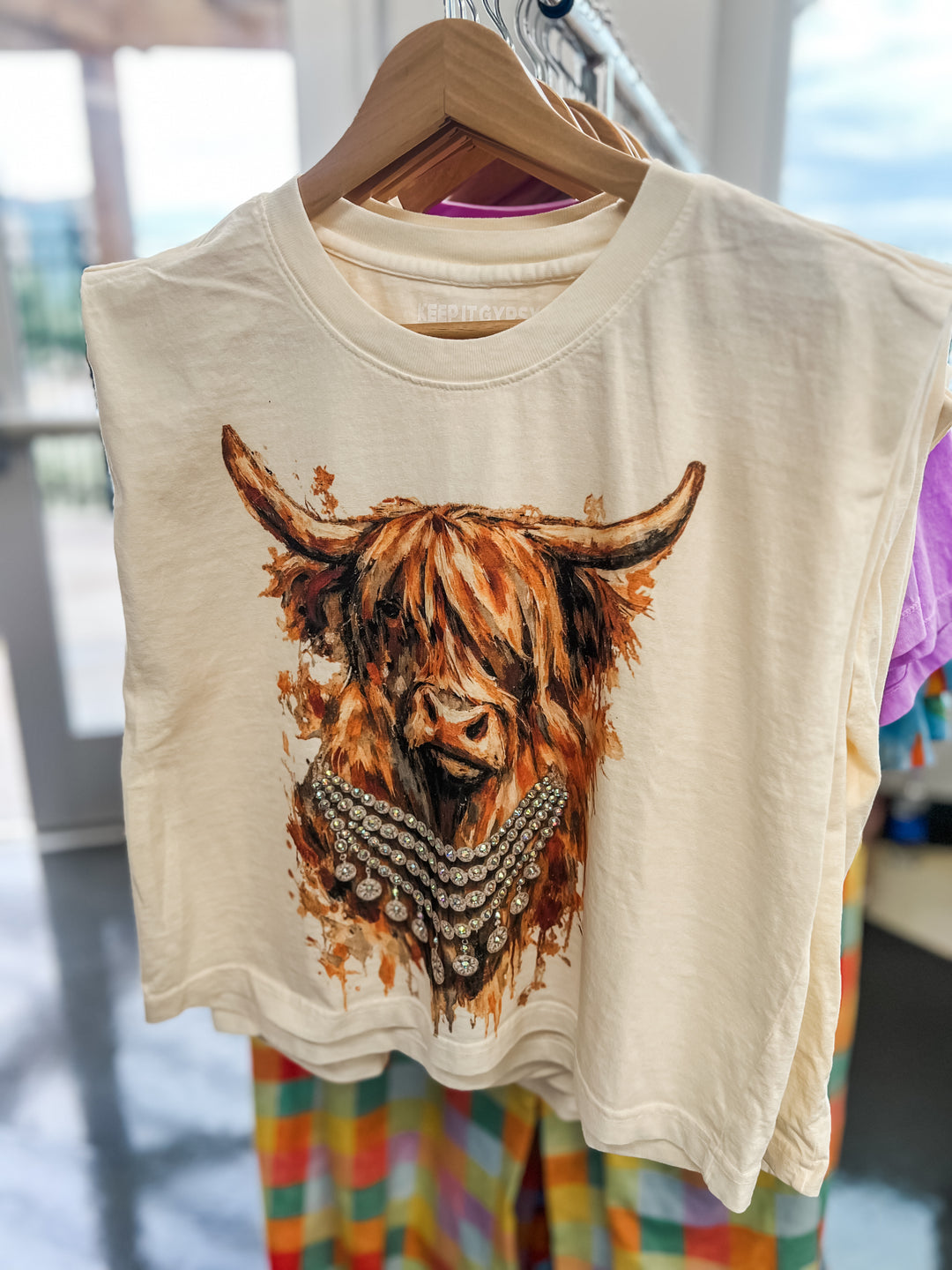 Beige t-shirt with a highland cow design on a hanger.