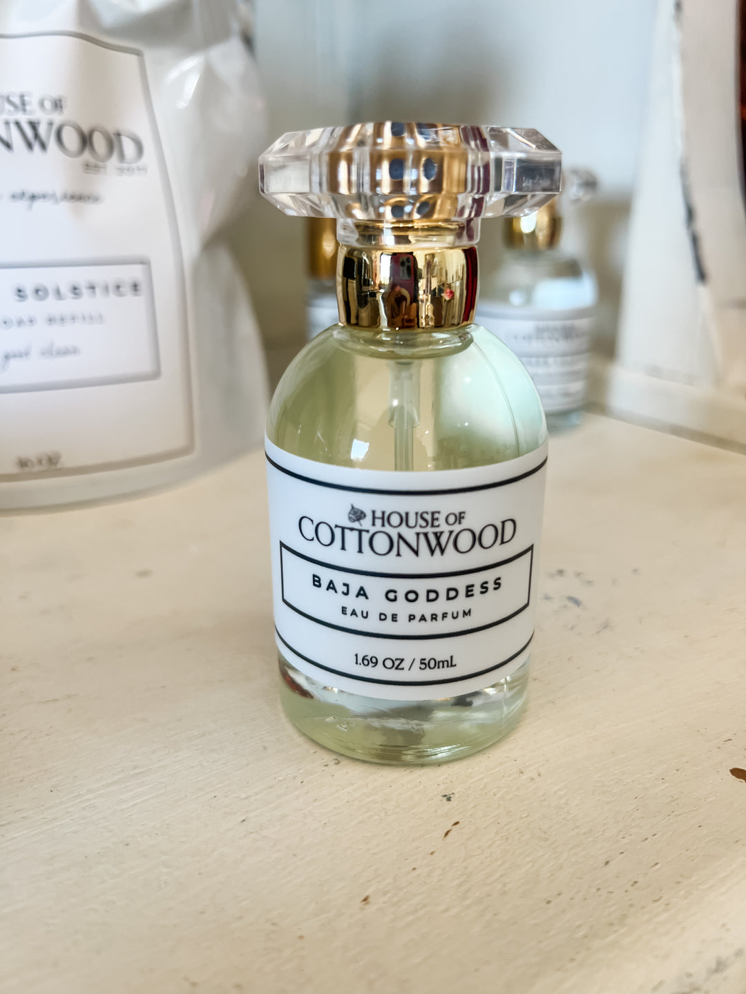 A 50mL glass perfume bottle with a clear faceted cap and a gold neck collar, featuring a white label that reads &
