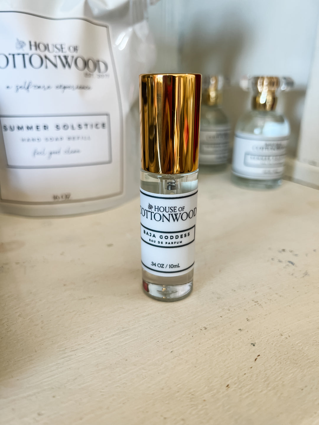 A small clear glass perfume bottle with a shiny gold cap and a white label reading &