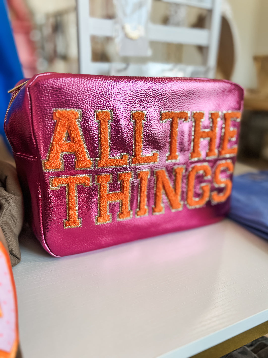 Pink pouch with 'ALL THE THINGS' text in orange on a blurred background