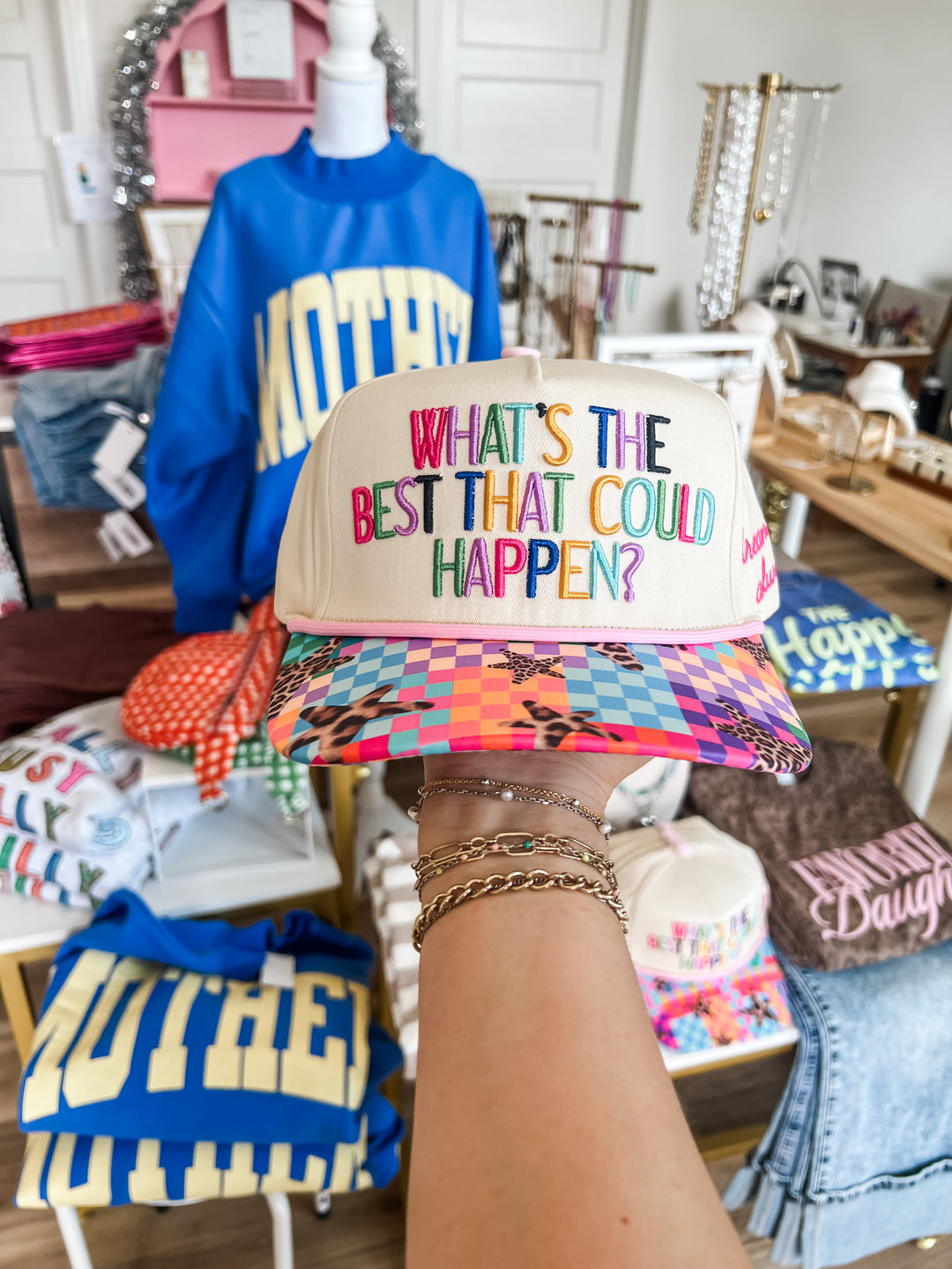 Colorful trucker hat with "What's the best that could happen?" text in a boutique store