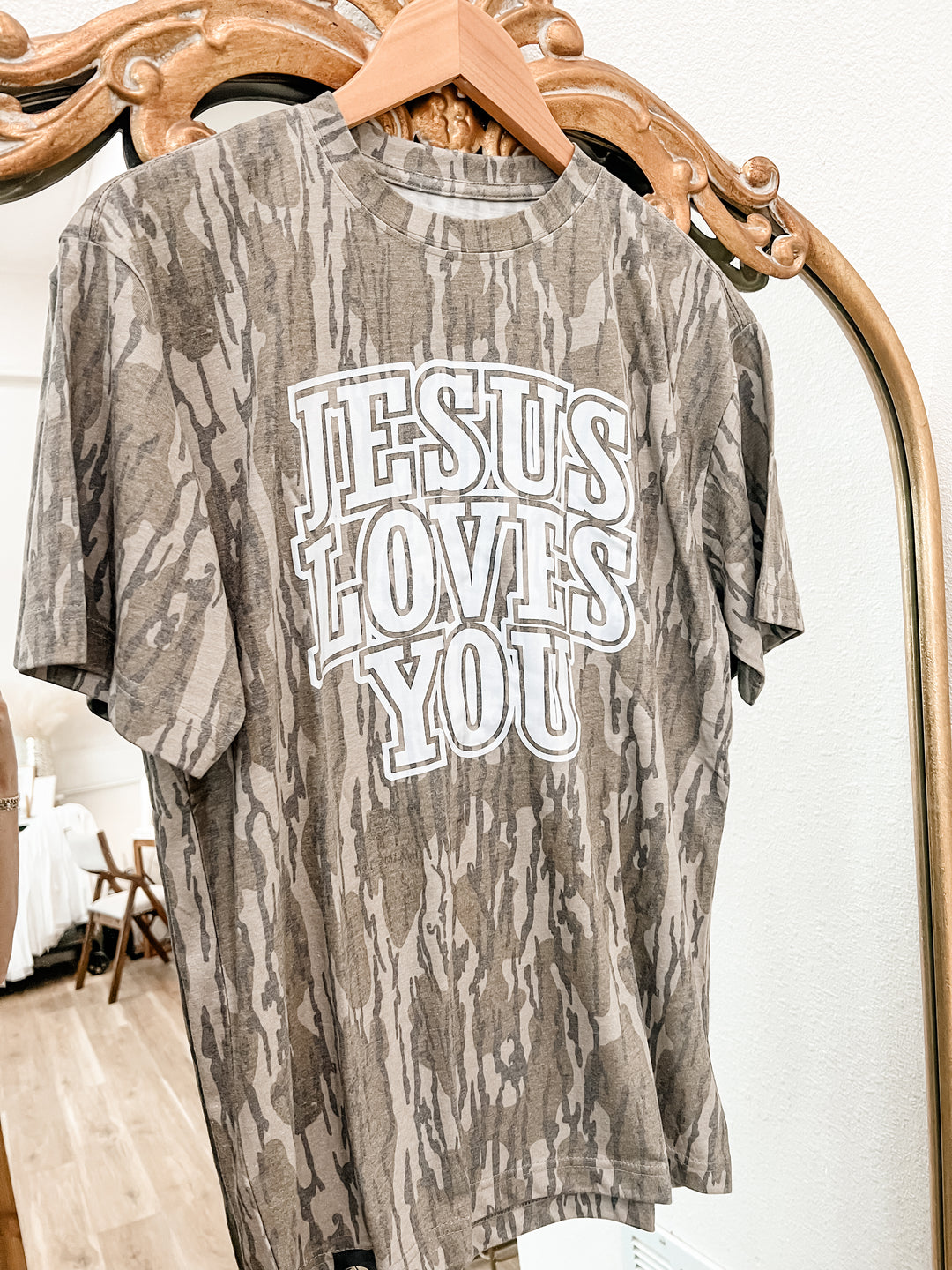 Camo patterned t-shirt with 'Jesus Loves You' text on a hanger.