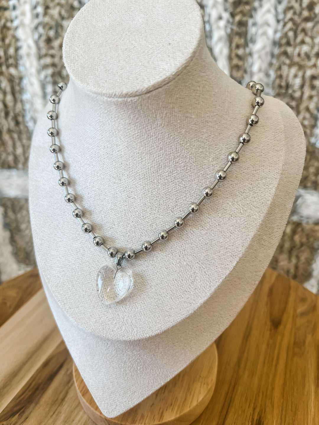 Necklace with clear pendant on a mannequin bust against a textured wall.
