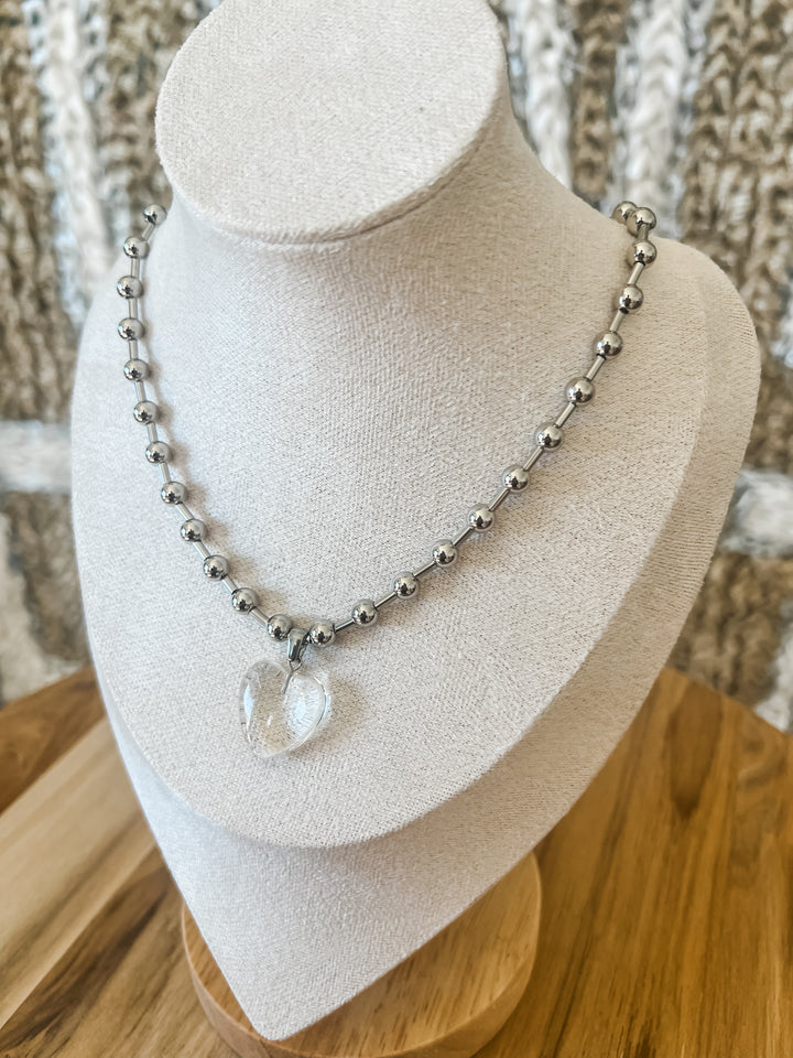 Necklace with clear pendant on a mannequin bust against a textured wall.