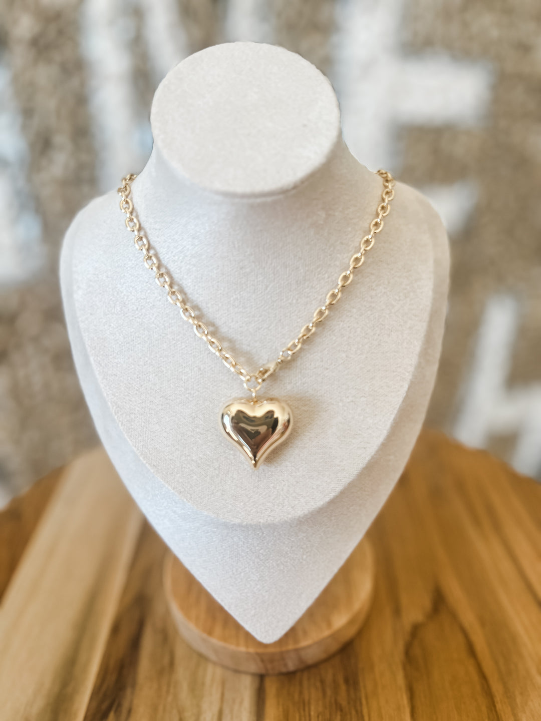 Gold heart-shaped pendant necklace on a white bust with a blurred background