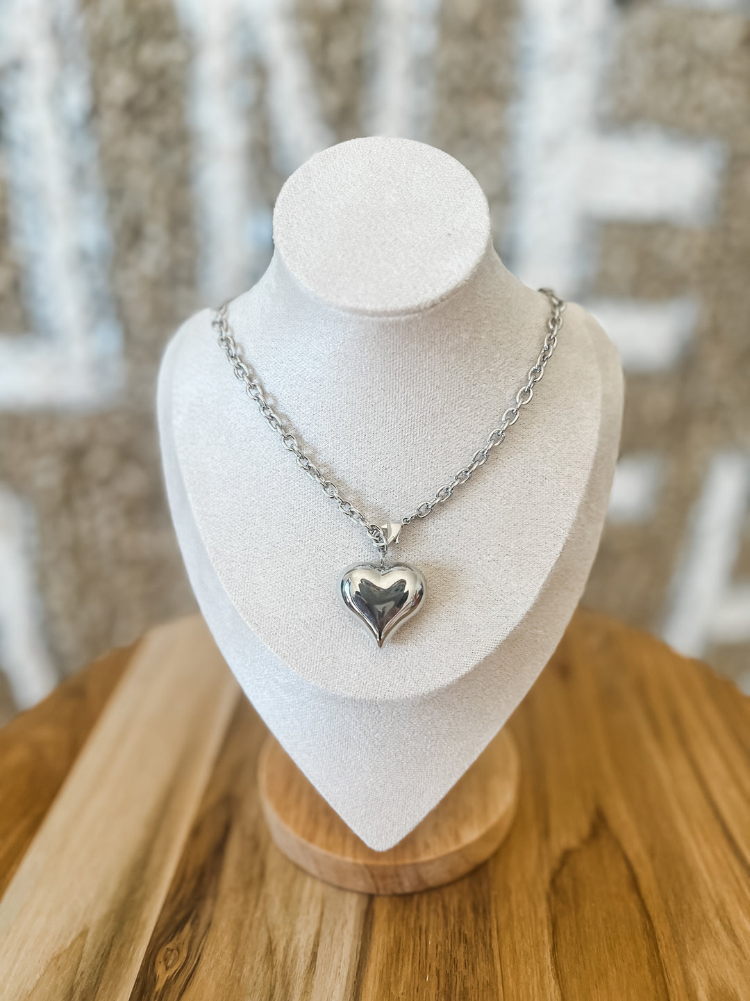 Silver heart-shaped pendant necklace on a mannequin bust with a blurred background