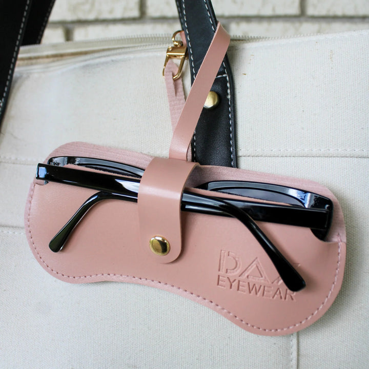 Pink sunglasses case with black sunglasses on a beige bag