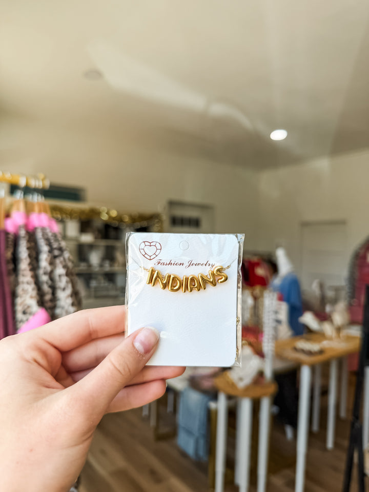 A hand holds a small white card featuring gold necklace with lettering that reads &