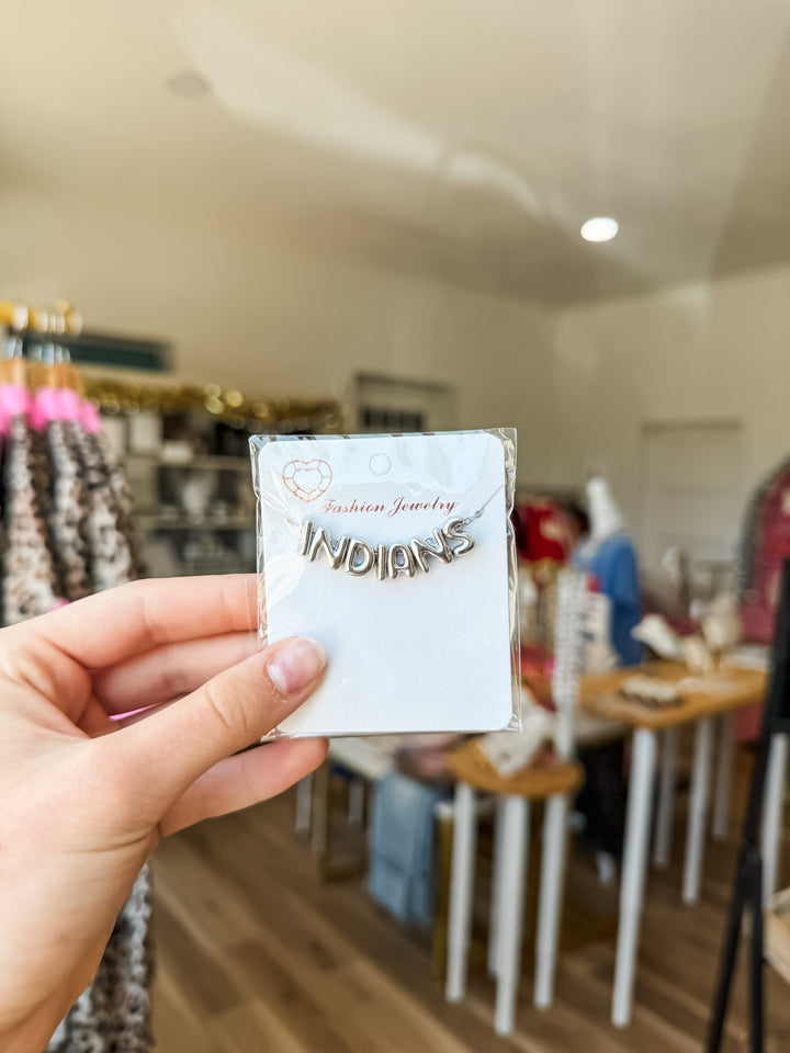 A hand holds a small silver-toned letter necklace spelling &