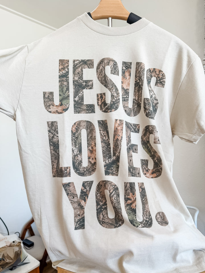A white short-sleeve t-shirt on a wooden hanger, featuring the text &