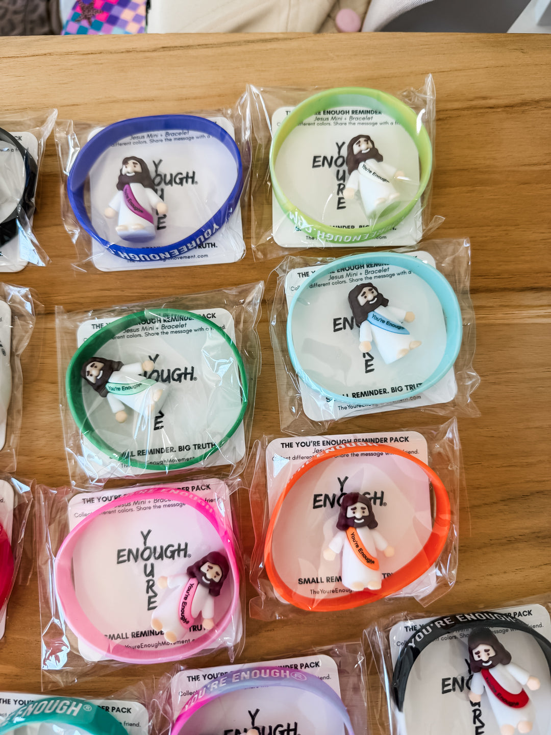 Several packaged mini Jesus figurines and bracelets on a wooden surface 