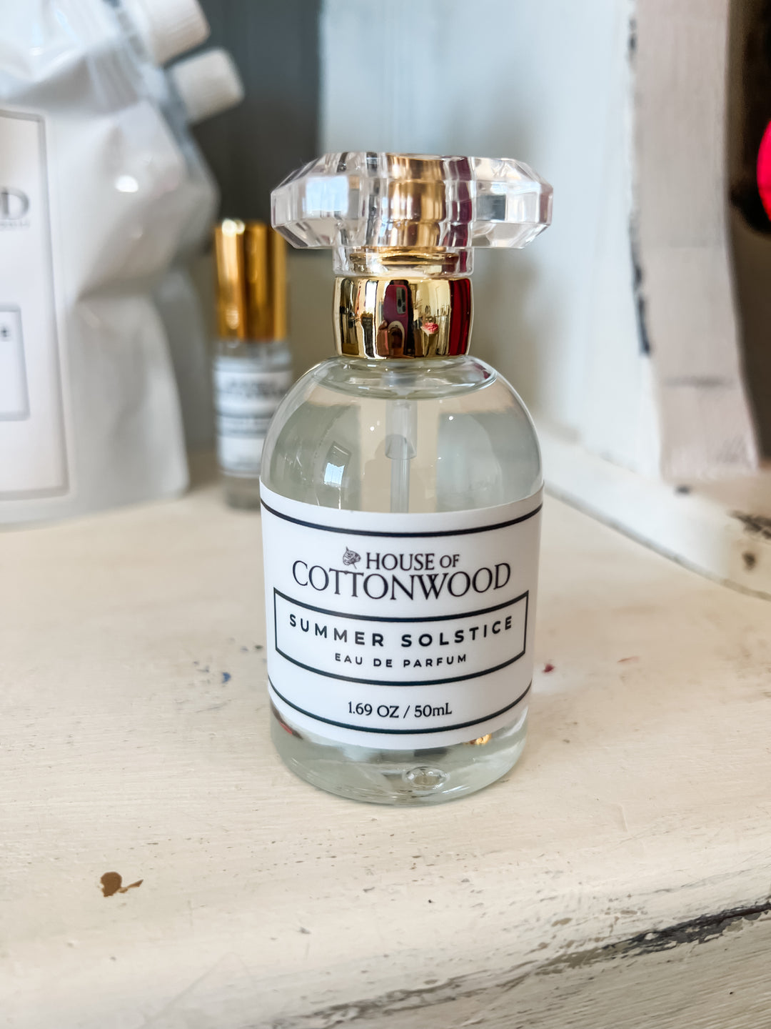 A 50mL clear glass perfume bottle with a faceted clear cap and a gold collar, featuring a white label that reads &