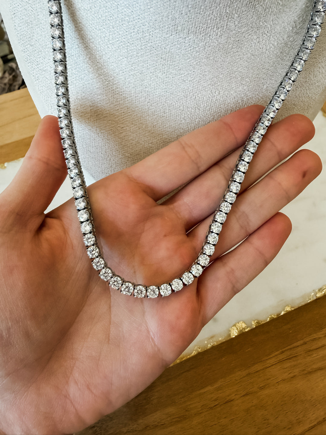 A close-up of a diamond tennis necklace held in a person&