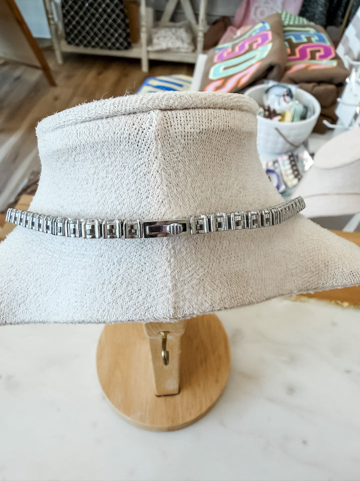 A silver tennis necklace displayed on a form stand, set on a wooden display base.