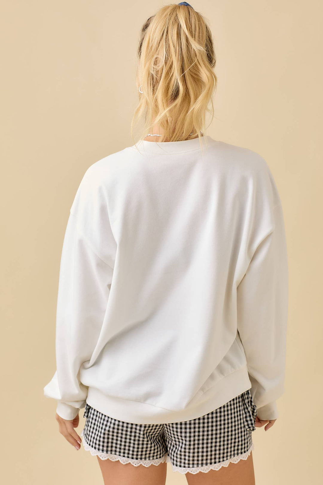 Person wearing a white sweatshirt and checkered shorts on a beige background