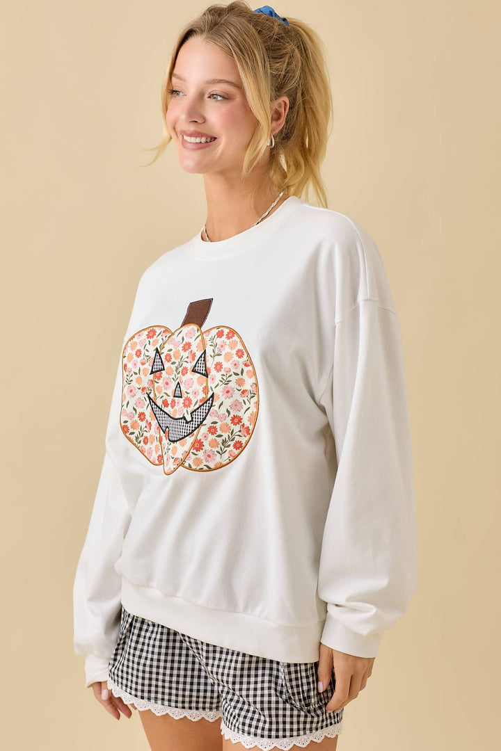 Woman wearing a white sweatshirt with a floral pumpkin design on a beige background