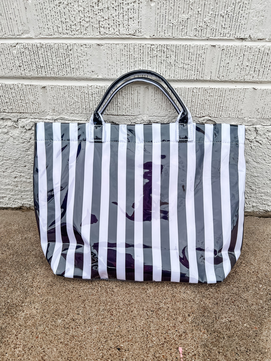 black and white striped tote on concrete with white brick background 