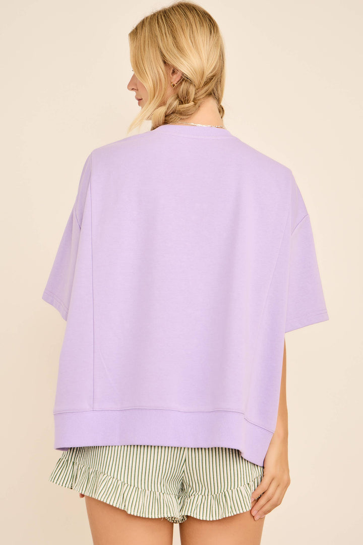 Person wearing a light purple oversized shirt with green and white striped shorts on a beige background