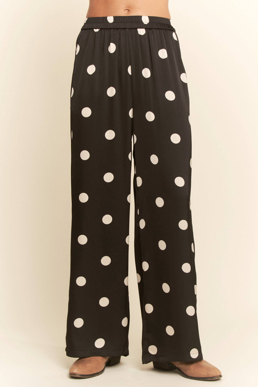 Black pants with white polka dots worn by a person on a beige background