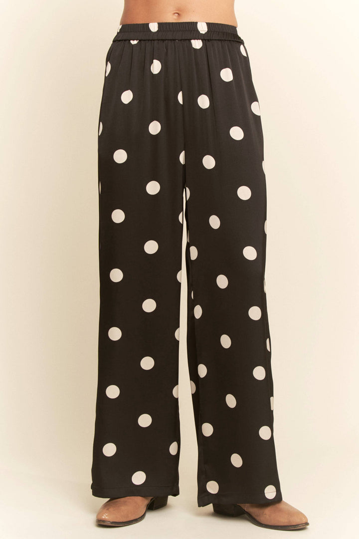 Black pants with white polka dots worn by a person on a beige background