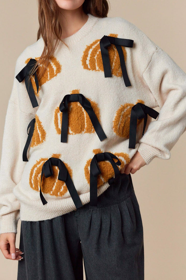Woman wearing a cream sweater with pumpkin patterns and black ribbons on a beige background